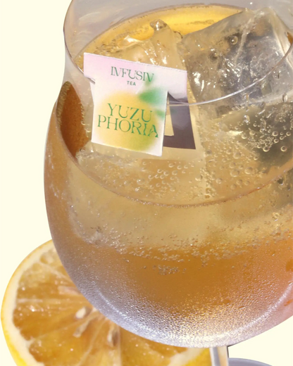 A glass of iced tea with a yuzu slice underneath and a Yuzuphoria teabag label clipped to the rim on a white background